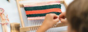 Girl weaving small rug with pattern at masterclass on weaving.