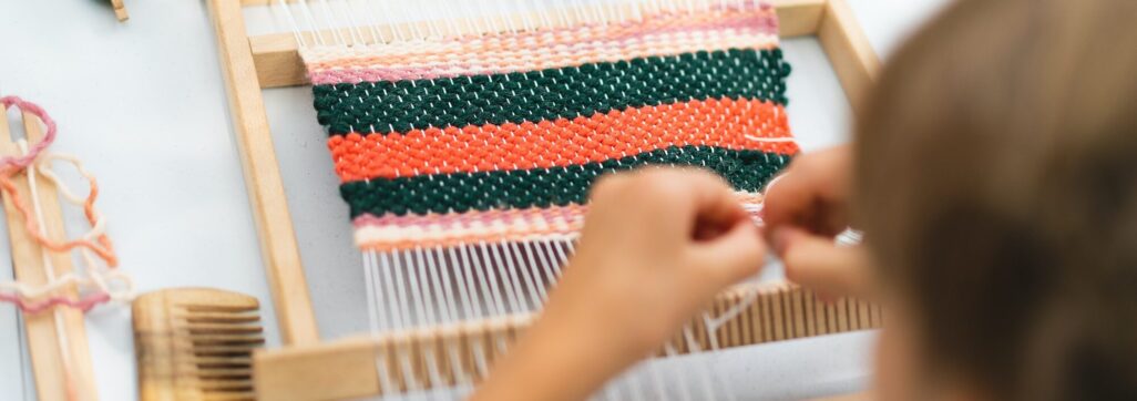 Girl weaving small rug with pattern at masterclass on weaving.